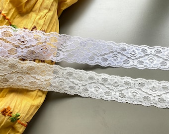 May include: Two white lace trims with a floral pattern. The lace is delicate and has a scalloped edge.