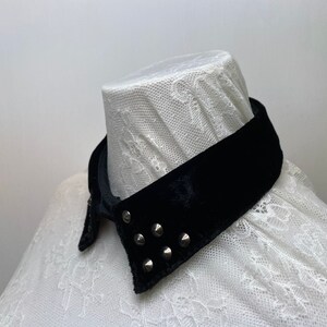 May include: A black velvet collar with silver studs. The collar is on a white lace shirt.