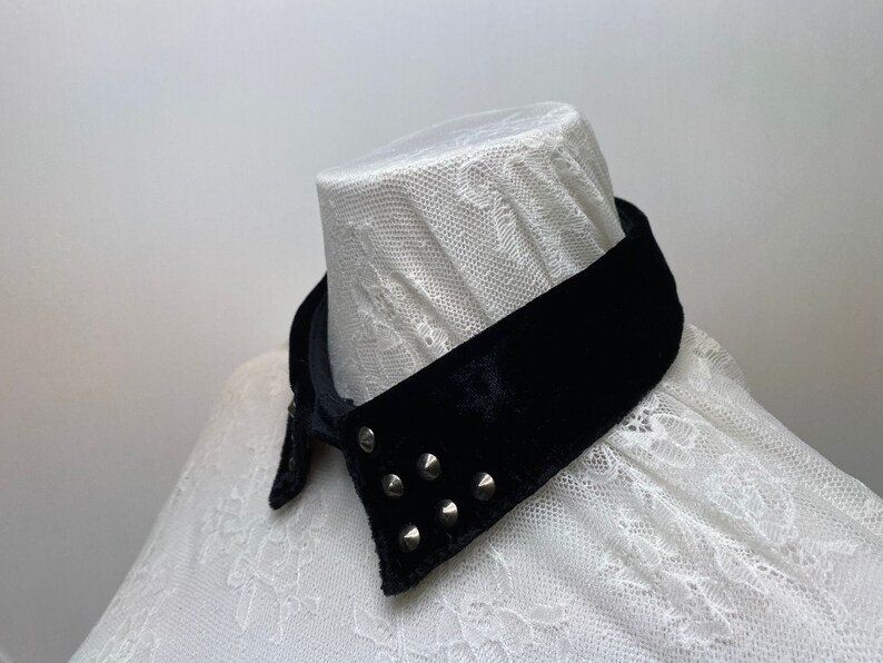 May include: A black velvet collar with silver studs. The collar is on a white lace shirt.