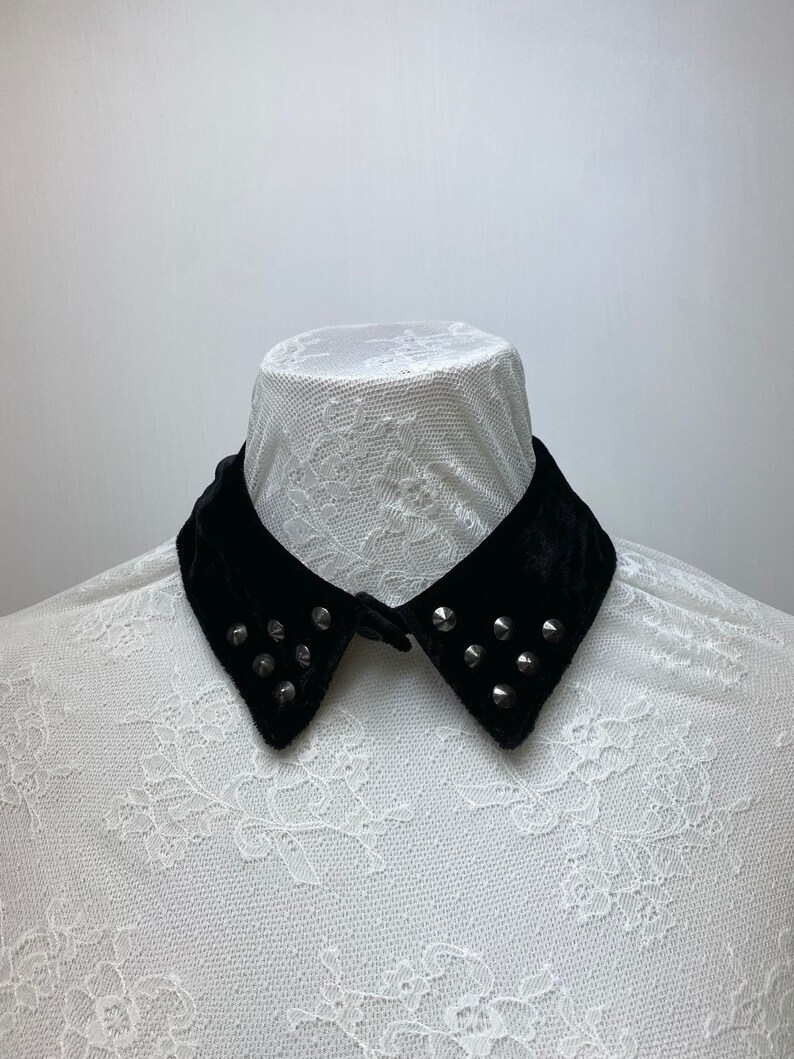 May include: A black velvet collar with silver studs. The collar is on a white lace shirt.