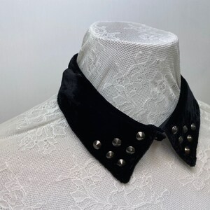 May include: A black velvet collar with silver studs. The collar is on a white lace shirt.
