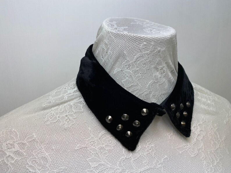 May include: A black velvet collar with silver studs. The collar is on a white lace shirt.