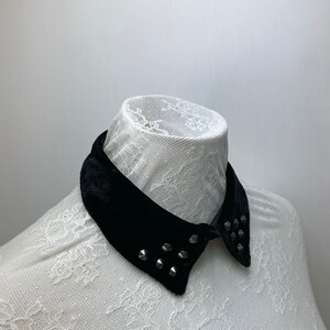May include: A black velvet collar with silver studs. The collar is on a white lace background.