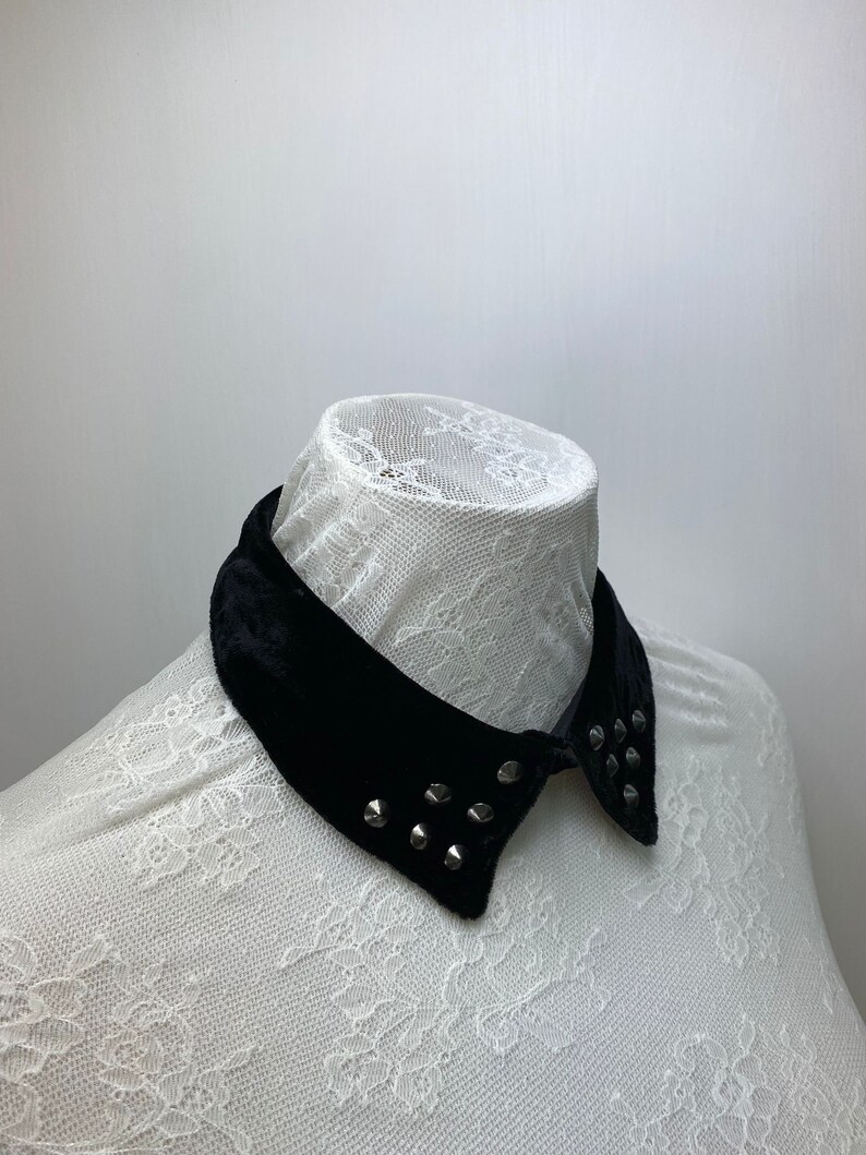 May include: A black velvet collar with silver studs. The collar is on a white lace background.