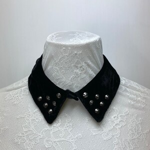May include: A black velvet collar with silver studs. The collar is on a white lace background.