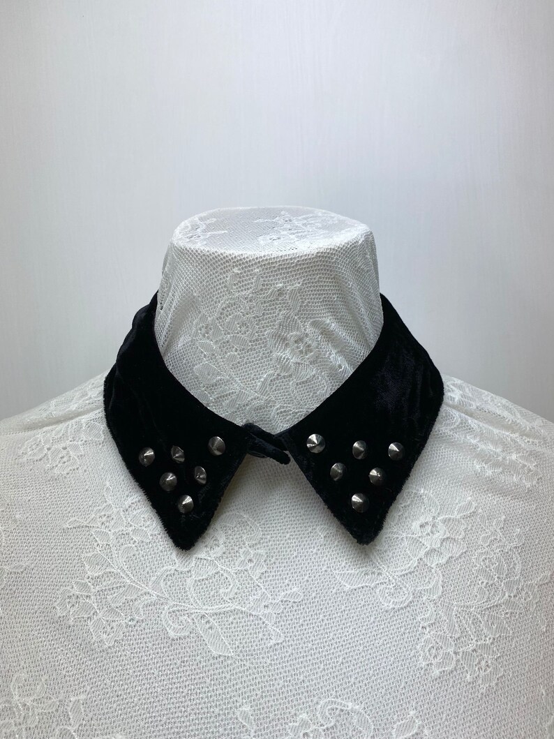 May include: A black velvet collar with silver studs. The collar is on a white lace background.