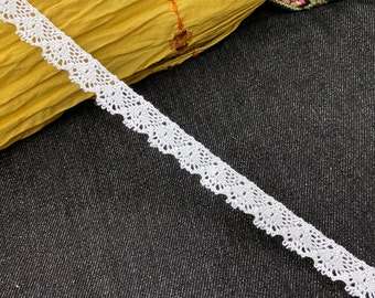May include: White crochet lace trim with a delicate scalloped edge. The lace is shown on a dark fabric background.