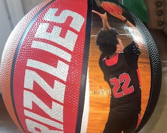May include: A red and black basketball with the word "Grizzlers" printed in silver on the side. A basketball player wearing a black jersey with the number 22 printed in red is pictured on the other side of the ball.