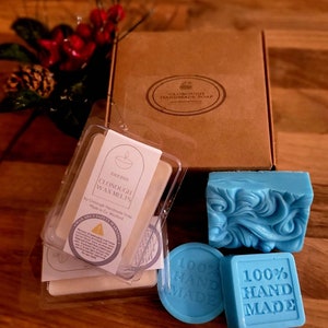 Puede incluir: Una caja de cartón marrón con una etiqueta blanca que dice "Clonough Handmade Soap" y una pastilla de jabón azul con un diseño de remolino. La caja también contiene dos ceras para fundir con una etiqueta blanca que dice "Clonough Wax Melts" y una pastilla de jabón azul con el texto "100% Hecho a Mano".