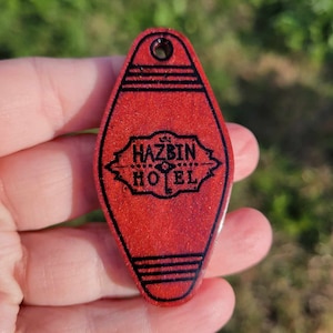 Può includere: Portachiavi di hotel rosso glitterato con scritta nera "The Hazbin Hotel".