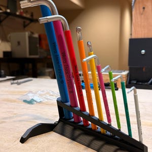 May include: A set of Wera Hex-Plus L-wrenches in a black stand. The wrenches are various colors, including blue, pink, red, orange, yellow, green, and gray. Each wrench has the "Wera Hex-Plus" logo printed on it.