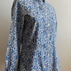 May include: A button-down shirt with a blue floral pattern. The long-sleeved shirt has a classic collar and white buttons. The fabric is a light blue and white with small blue flowers.