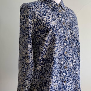 Peut inclure: Chemise &agrave; manches longues bleu marine avec un motif floral cr&egrave;me. La chemise a un col classique et des boutons en bois. Le tissu semble l&eacute;ger, id&eacute;al pour les temp&eacute;ratures plus chaudes. La chemise est pr&eacute;sent&eacute;e sur un mannequin.