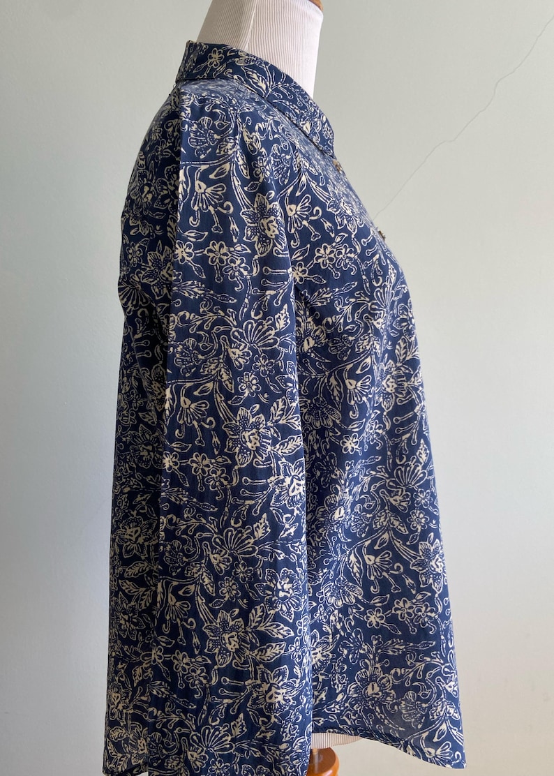 Peut inclure: Chemise bleu marine &agrave; boutons avec un motif floral cr&egrave;me. La chemise &agrave; manches longues est pr&eacute;sent&eacute;e sur un mannequin. Le tissu a un aspect doux et fluide, et le motif floral est r&eacute;p&eacute;t&eacute; sur tout le v&ecirc;tement.
