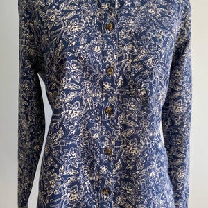 Peut inclure: Chemise &agrave; manches longues bleu marine avec un motif floral cr&egrave;me. La chemise a un col classique et des boutons en bois. Le motif floral comprend des feuilles et des fleurs.