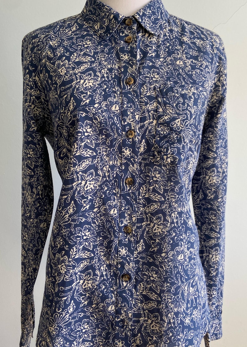 Peut inclure: Chemise &agrave; manches longues bleu marine avec un motif floral cr&egrave;me. La chemise a un col classique et des boutons en bois. Le motif floral comprend des feuilles et des fleurs.
