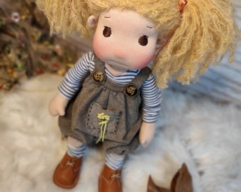 May include: A handmade doll with blonde hair in pigtails, wearing a blue and white striped shirt, brown overalls with a flower design, and brown shoes.