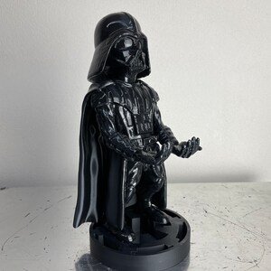 May include: A black Darth Vader phone stand. The stand is shaped like Darth Vader and has a base that resembles the Death Star.