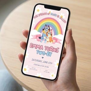 May include: A smartphone displaying a digital birthday invitation with a light pink background, white daisy pattern, a rainbow, and Bluey characters. Text reads: This episode of Bluey is called Emma turns two-ey, Saturday, June 6th, 04:30 PM.