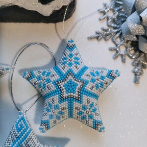 May include: A blue and white beaded star ornament with a snowflake pattern. The star is hanging from a silver string.