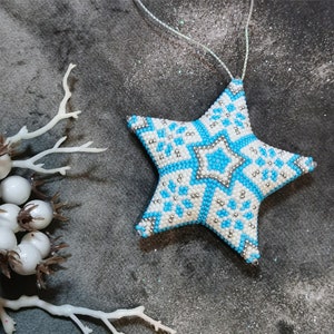 May include: A blue and white beaded star ornament with a snowflake pattern. The star is hanging from a white string.