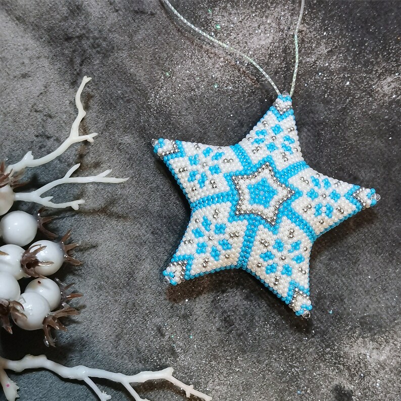 May include: A blue and white beaded star ornament with a snowflake pattern. The star is hanging from a white string.