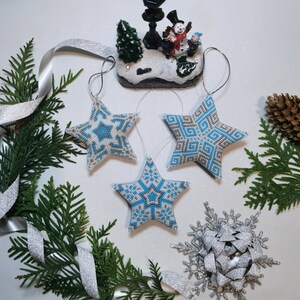 May include: Three blue and white beaded star ornaments with a snowflake and a winter scene figurine in the background.