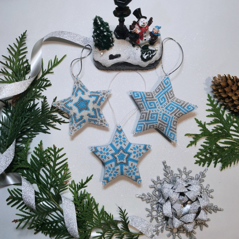 May include: Three blue and white beaded star ornaments with a snowflake and a winter scene figurine in the background.