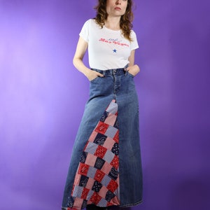 May include: A woman wearing a white t-shirt with the text "Old Las Vegas" and a blue denim skirt with a red, white and blue patchwork design.