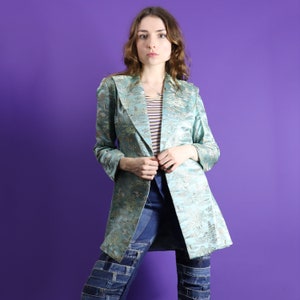 May include: A light blue jacket with a floral pattern and a long, flowing design. The jacket is worn over a striped shirt and blue jeans.