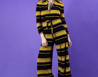 May include: A striped jumpsuit with a black, yellow, and red color scheme. The jumpsuit has a collared neckline, long sleeves, and a wide-leg silhouette.