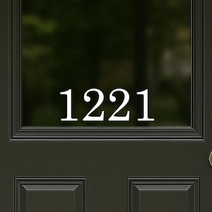 May include: A black front door with the white house number "1221" displayed in the glass window. The door has a brass doorknob and is framed by white trim. A black lantern hangs on the left.