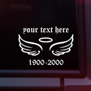 May include: White decal showing angel wings and a halo, with the text "your text here" above and "1900-2000" below. The decal is displayed on a dark surface, possibly a car window.