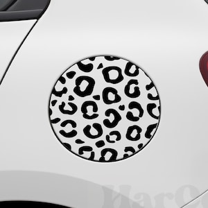 May include: A black and white leopard print decal applied to a white car. The circular decal is centered on the car's fuel door, featuring a repeating pattern of black spots against a white background. The car's red tail light is visible.
