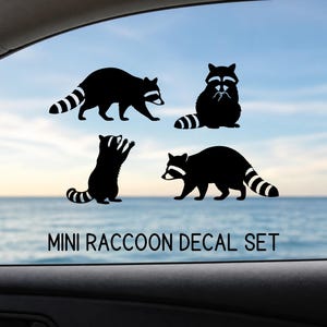 May include: A set of four black raccoon decals in various poses, including standing, walking, and sitting. The decals have white and black striped tails and are displayed on a car window with the text "MINI RACCOON DECAL SET".