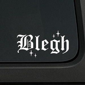 以下が含まれることがあります： ゴシック体で「Blegh」と書かれた白いビニールデカール。小さなスターバーストで装飾されています。黒い車の窓に貼られており、クリーンでミニマルなデザインです。