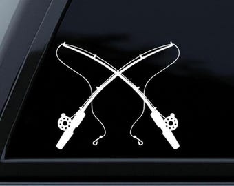 May include: White vinyl decal of two crossed fishing rods, featuring reels and curved lines. The rods are positioned against a black background, creating a contrasting silhouette. Ideal for car windows or outdoor gear.