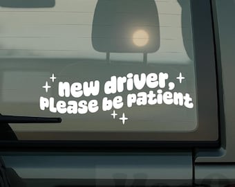May include: White vinyl decal for a car window with the text "new driver, Please be patient" in a playful font. The decal includes star-shaped accents. The sticker is designed to be applied to the exterior of a vehicle.