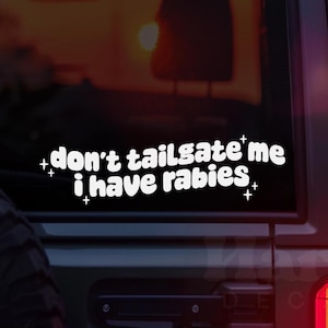 Puede incluir: Pegatina de vinilo blanco con el texto "don't tailgate me i have rabies" en una fuente redondeada. La pegatina está en la ventana trasera de un coche.