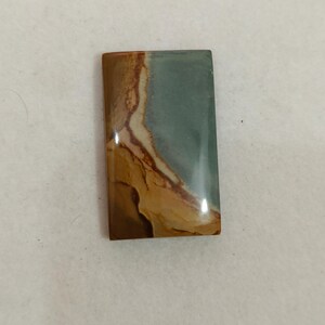 May include: A rectangular polished gemstone cabochon featuring a smooth surface with a distinct color pattern. The stone displays a blend of muted sage green, creamy beige, and deep brown tones arranged in flowing, organic, layered bands.