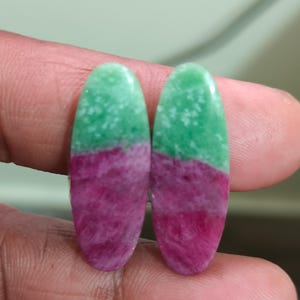 May include: Two oval-shaped cabochons featuring a distinct color split. The top half of each stone is a vibrant, speckled light green, while the bottom half is a deep, textured magenta-pink. These polished gemstones have a smooth, glossy finish.