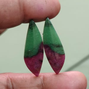 Pode incluir: Dois cabochões em forma de marquise com uma separação de cores distinta entre o verde vibrante e o magenta-rosa profundo. Estas pedras polidas exibem inclusões minerais naturais e uma superfície lisa e curva.