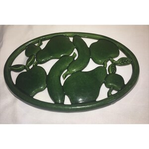 May include: A green ceramic oval serving platter with raised fruit and vegetable designs. The platter features pears, apples, and cucumbers in a glossy finish. The rim of the platter is also green.