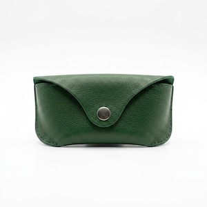 May include: A forest green leather glasses case with a textured surface, featuring a curved flap closure secured by a single silver-toned metal snap button. The case has visible stitching along the edges and a structured, rounded rectangular shape.