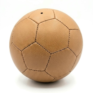 May include: A tan-colored soccer ball constructed from textured panels stitched together with dark thread. The ball features a classic hexagonal and pentagonal pattern with a small, circular inflation valve visible near the top center of the sphere.