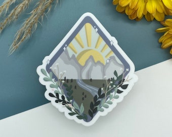 May include: A white diamond-shaped sticker with a mountain range, a sun, and green foliage. The sun is yellow with orange rays. The mountains are gray and purple. The foliage is green and white.