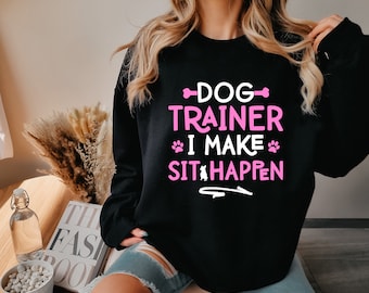 May include: Black sweatshirt with the text "DOG TRAINER I MAKE SIT HAPPEN" in pink and white lettering.