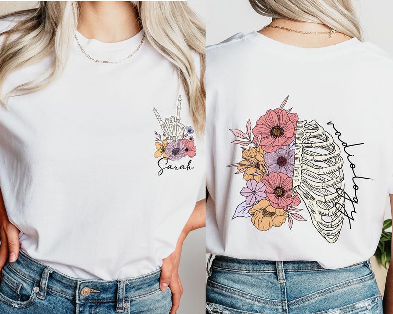 Pode incluir: Camiseta branca com um design floral e uma m&atilde;o de esqueleto fazendo o sinal de linguagem de sinais 'Eu te amo'. O texto 'Sarah' est&aacute; abaixo do design. A parte de tr&aacute;s da camiseta tem um design floral com uma caixa tor&aacute;cica e o texto 'radiologia'.