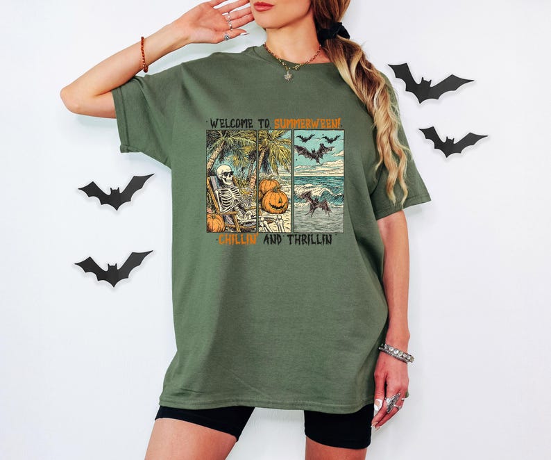 May include: Olive green t-shirt with a graphic design featuring a skeleton relaxing on a beach, pumpkins, bats, and the text "WELCOME TO SUMMERWEEN, CHILLIN AND THRILLIN". The shirt is worn by a person.