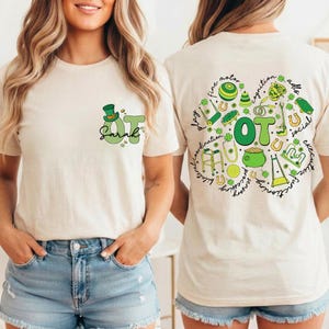 May include: Beige t-shirt with a green and white design. The front features the text "OT Sarah" with a leprechaun hat and shamrock. The back has a green clover design with the letters "OT" and related words like "play" and "social".